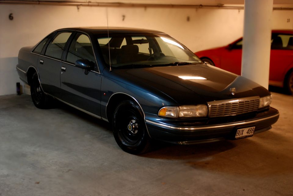 Dark teal 1990s full-size sedan on black steel wheels in an underground garage