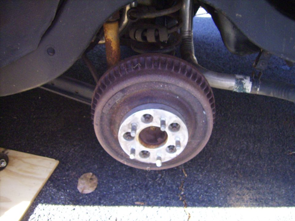 Rusty brake drum with aluminum wheel adapter installed, wheel removed, under rear of car