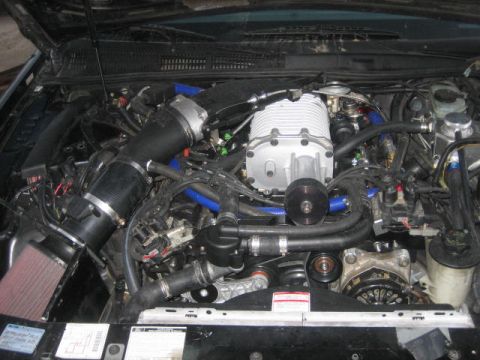 1996 Ford Thunderbird - The engine bay of a vehicle is shown with a prominent supercharger and various hoses and components.
