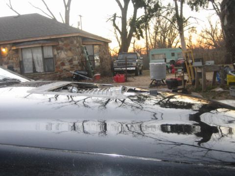 1996 Ford Thunderbird - A close-up of a car's hood scoop is visible in the foreground, with a house and other vehicles in the background.