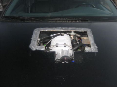 1996 Ford Thunderbird - A supercharger is visible through a custom opening in the hood of a car.