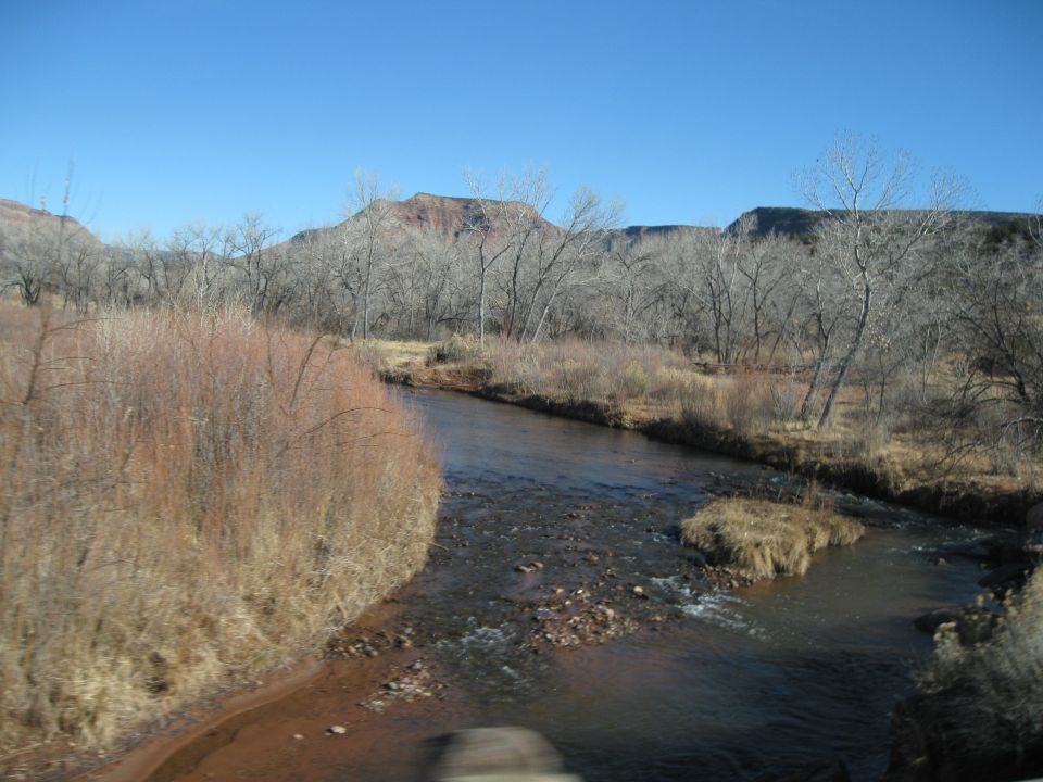 River flowing through a landscape with bare trees and hills under a clear blue sky