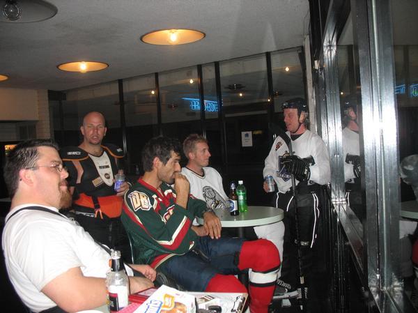 Group of hockey players in jerseys and gear relaxing with drinks at tables in a lounge