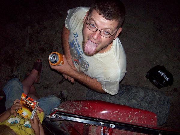 Man with glasses and beard sticking his tongue out, holding an orange can. A child holds a Matchbox box