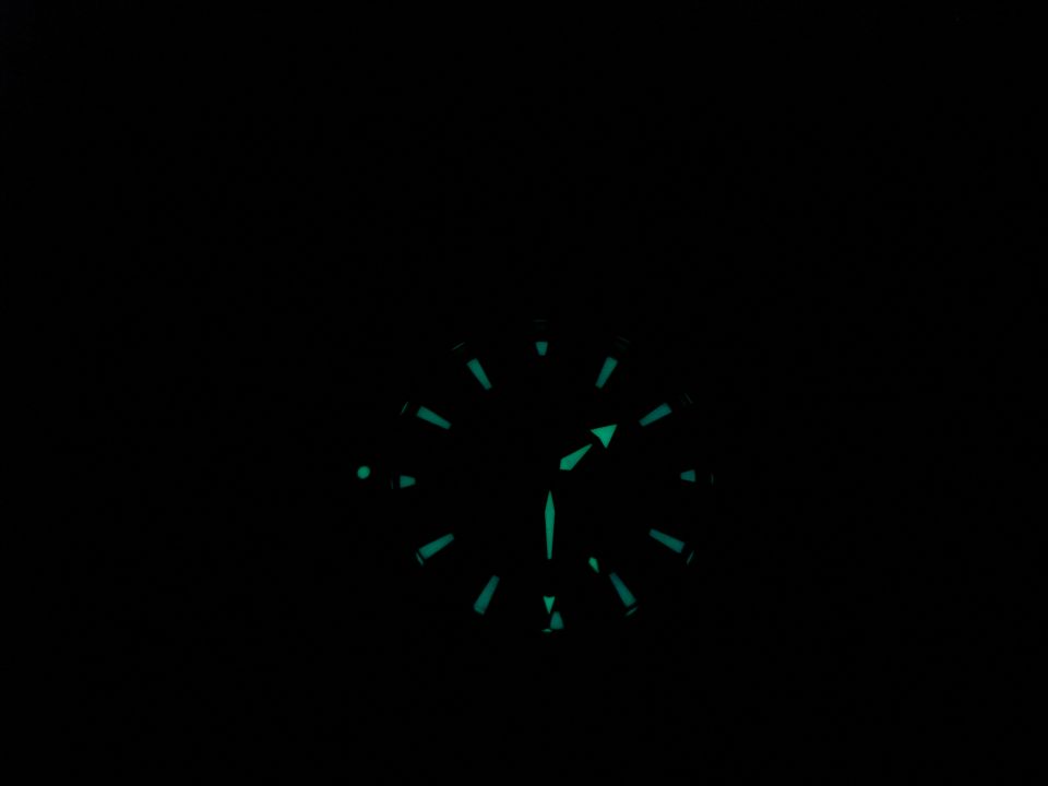 Watch face with luminous green markers and hands against a black background