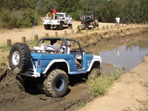 1989 Ford Bronco - This modified SUV tackles a challenging muddy obstacle course with other vehicles nearby.