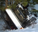 1989 Ford Bronco - Vehicle overturned in snow, partially obscured by trees and snow.