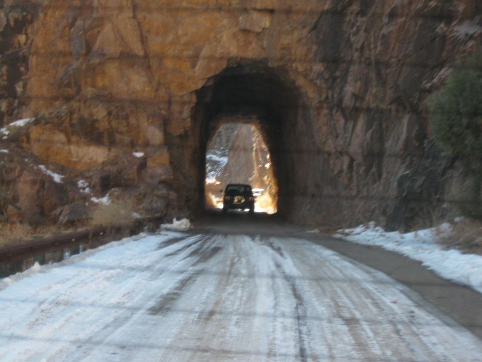 Dark SUV seen from behind driving on a snow-covered road through a rock tunnel