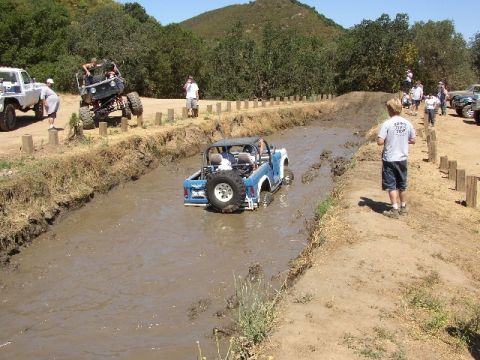 1989 Ford Bronco - Off-road vehicles navigate a muddy track during an event.