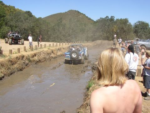 1989 Ford Bronco - Off-road vehicles navigate a muddy track with spectators observing the action.
