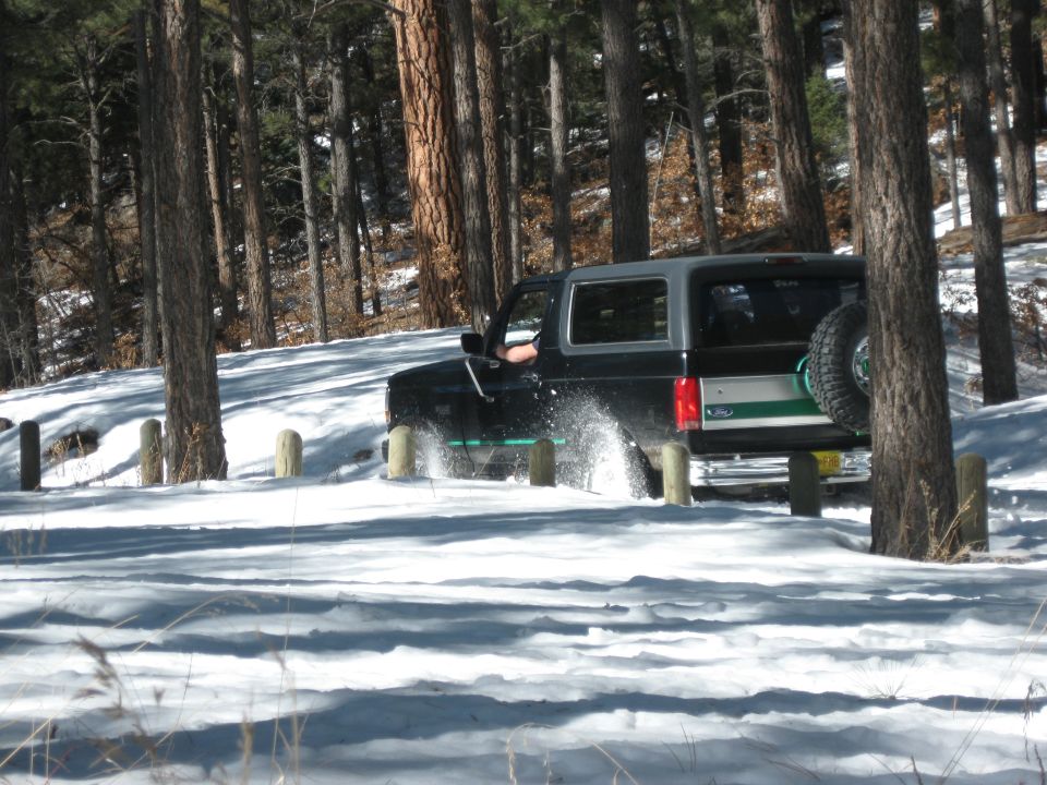 1993 Ford Bronco driving through snow in a wooded area, kicking up snow