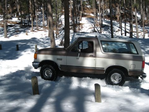 1993 Ford Bronco - A two-tone brown and white 1993 Ford Bronco navigates a snowy, wooded area.