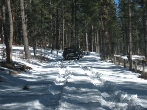 1993 Ford Bronco - A black SUV navigates a snow-covered road through a dense forest.