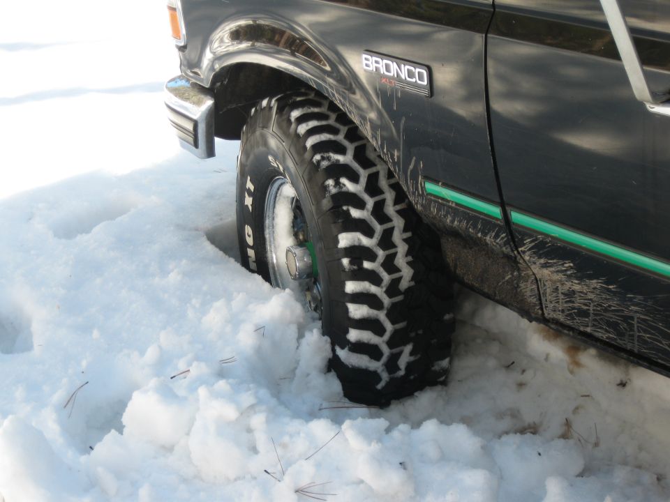 Close-up of a 1993 Ford Bronco's front tire stuck in snow