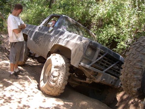 1989 Ford Bronco - This heavily modified pickup truck is shown tackling a challenging off-road course, with a second tire visible to the right.