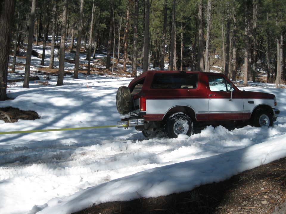 1993 Ford Bronco stuck in snow, being pulled by a yellow strap