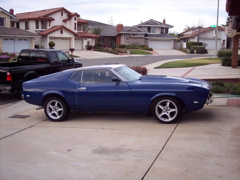 1971 Ford Mustang - A blue coupe is parked in a suburban driveway next to a black pickup truck.