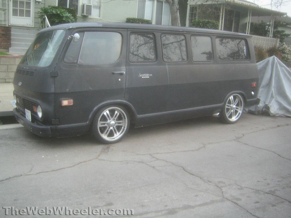 Black panel van with custom wheels parked on a street