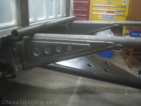 1990 Ford Bronco - close-up of a welded tubular steel suspension or chassis arm with drilled gusset plates inside a garage with tool chests behind.