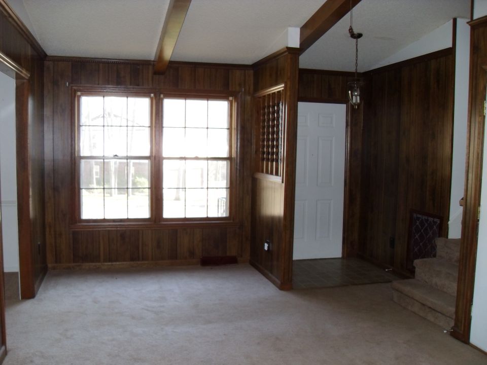 Interior room with wood paneled walls, carpet, two windows, a white door, and stairs