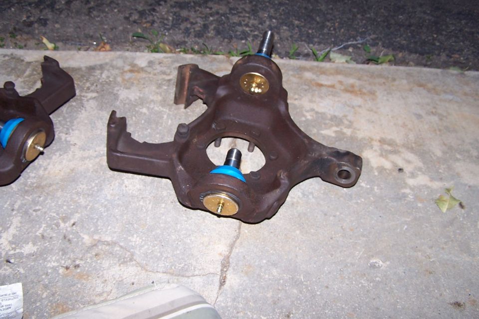 Two rusty ball joint assemblies with blue dust boots and gold caps on a concrete surface