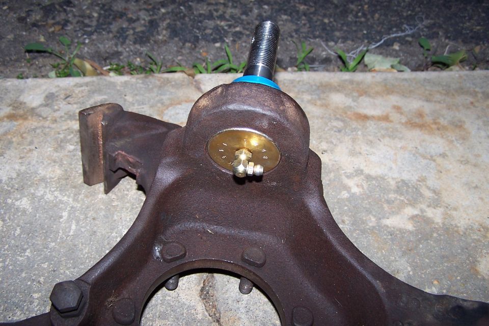 Close-up of a rusty ball joint assembly with a brass cap and grease fitting