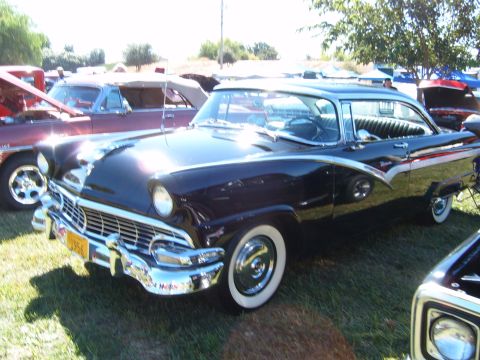 1956 Ford Fairlane - Black 1956 Ford Fairlane coupe with chrome trim and whitewall tires at an outdoor car show.