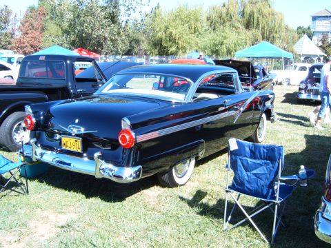 1956 Ford Fairlane - A classic black Ford Fairlane Crown Victoria is displayed at an outdoor event with other vehicles and tents.