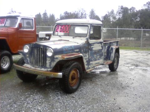 1989 Ford Bronco - A distressed pickup truck, possibly a Jeep Willys, is parked next to another vehicle, with a price tag visible in the windshield.