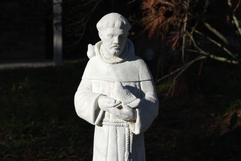 1901 Yugo Vega - A statue of a monk holding a bird is shown outdoors with trees in the background.