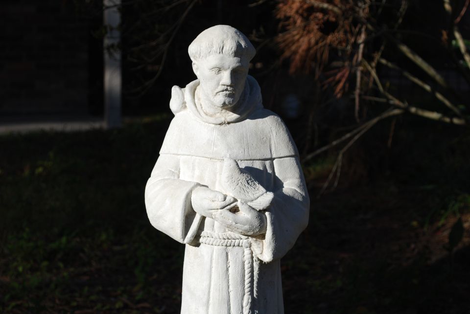 stone statue of a robed man with a beard holding a bird in his hands