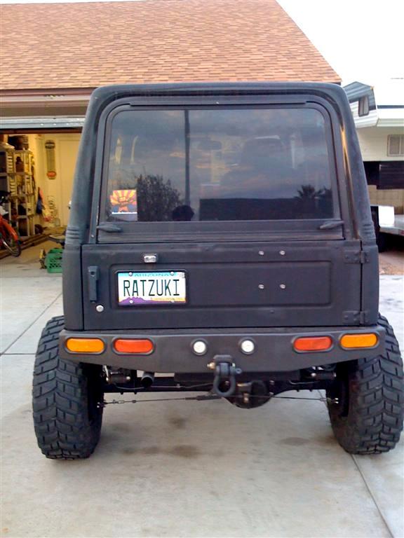 1987 Suzuki Samurai rear view with custom bumper and large tires. License plate reads RATZUKI