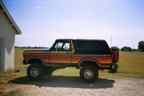 1979 Ford Bronco - A lifted Ford Bronco with a distinctive stripe pattern sits parked on a gravel driveway under a clear blue sky.