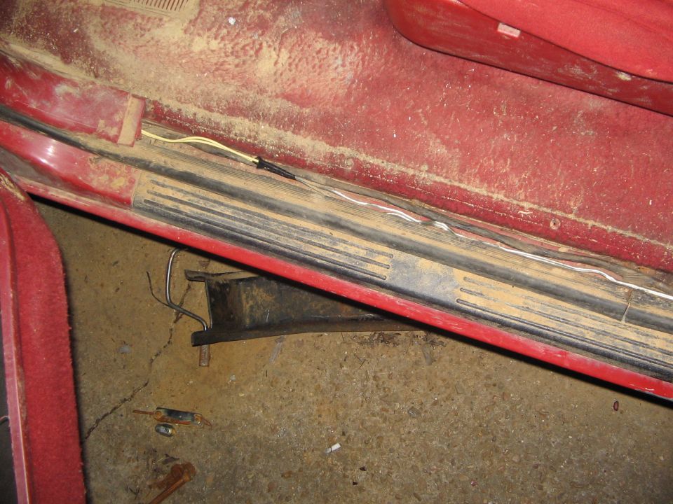 Red Bronco door sill with black scuff plate loosened and exposed wiring along the rocker, garage floor below