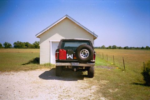 1979 Ford Bronco - Rear view of a black Ford Bronco parked in front of a garage with a rural landscape in the background.