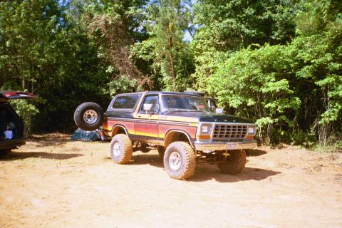 1979 Ford Bronco - Lifted 1978 Ford Bronco parked in a dirt lot with trees in the background. Another vehicle is partially visible.