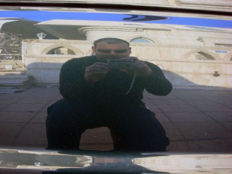 2000 Mitsubishi Montero - A man kneels to take a photo of his reflection in the shiny exterior of a dark-colored vehicle.