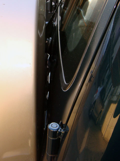 2000 Mitsubishi Montero - Close-up view of a door hinge and window trim on a dark-colored vehicle.