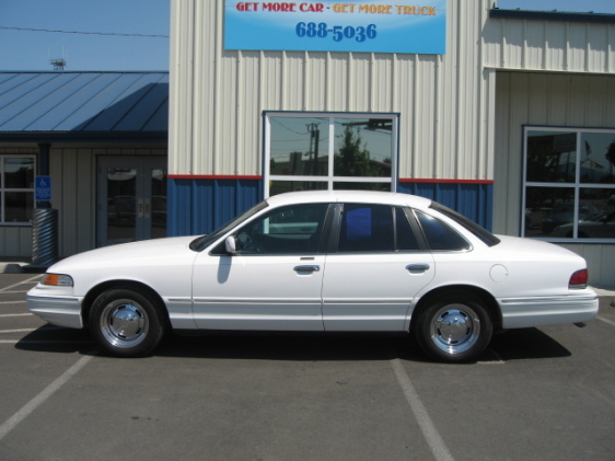 White Ford Crown Victoria sedan parked in front of a car dealership building