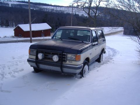 1988 Ford Bronco - Ford Bronco sits in a snowy landscape next to a red barn.