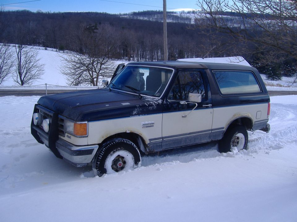 Two-tone Ford Bronco stuck in deep snow, front bull bar visible