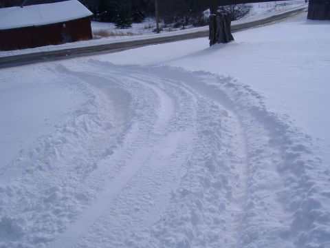1988 Ford Bronco - Tire tracks mark a path through the snow, leading away from a red barn and towards a road.