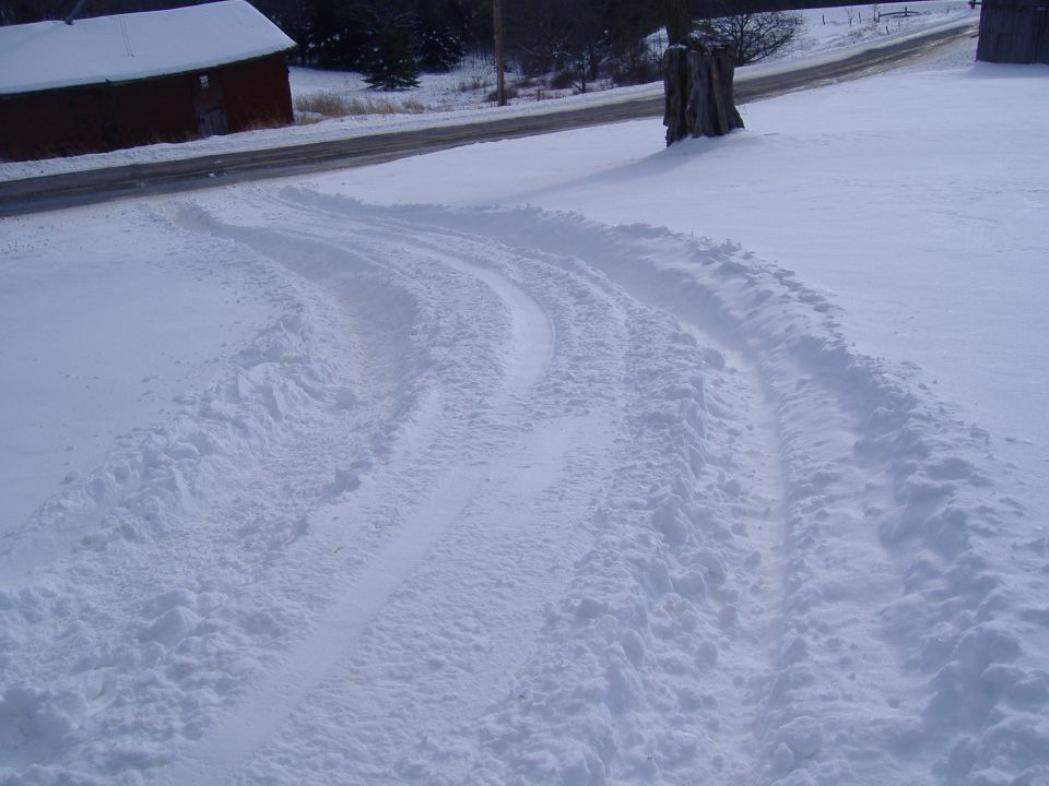 Tire tracks in snow leading away from a red barn