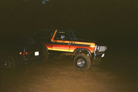 1979 Ford Bronco - A lifted Ford Bronco with distinctive side striping is parked outdoors in the dark next to another vehicle.
