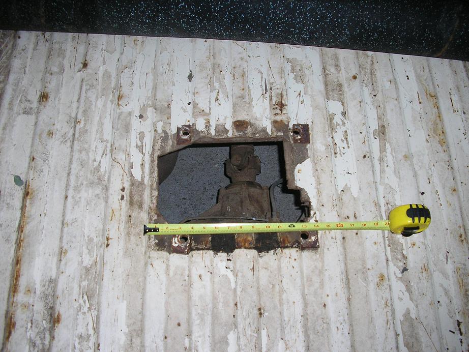Tape measure across a rectangular hole cut in a worn white truck bed floor