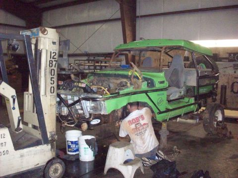 1978 Ford Bronco - A custom green off-road vehicle is undergoing modifications in a workshop, with a mechanic attending to its undercarriage.