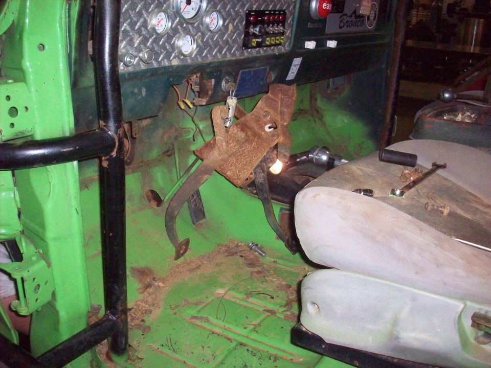 Interior of a green vehicle with a roll cage, diamond plate dash, and rusty pedals. A "Bronco" badge is visible