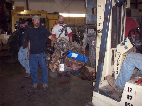 1978 Ford Bronco - Forklift moves an engine block in a workshop setting with several people observing.