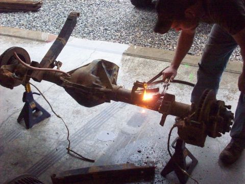1978 Ford Bronco - A person uses a cutting torch on a vehicle's rear axle assembly, with the Supermotors.net watermark in the corner.