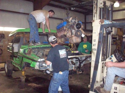 1978 Ford Bronco - Mechanics are installing an engine into a green vehicle with the help of a forklift.